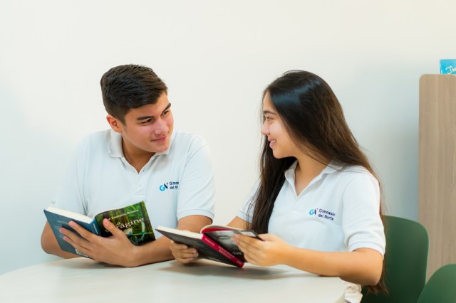 Jóvenes en biblioteca con libro abierto sonriendo